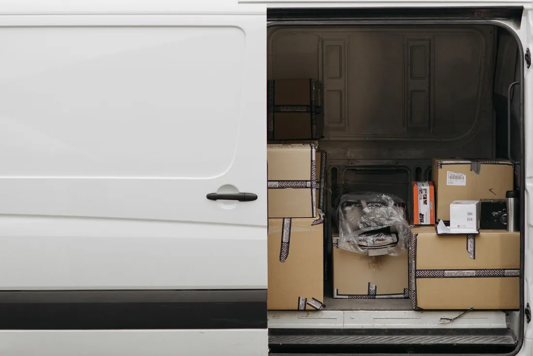 Cardboard parcels inside the open side door of a white delivery van.